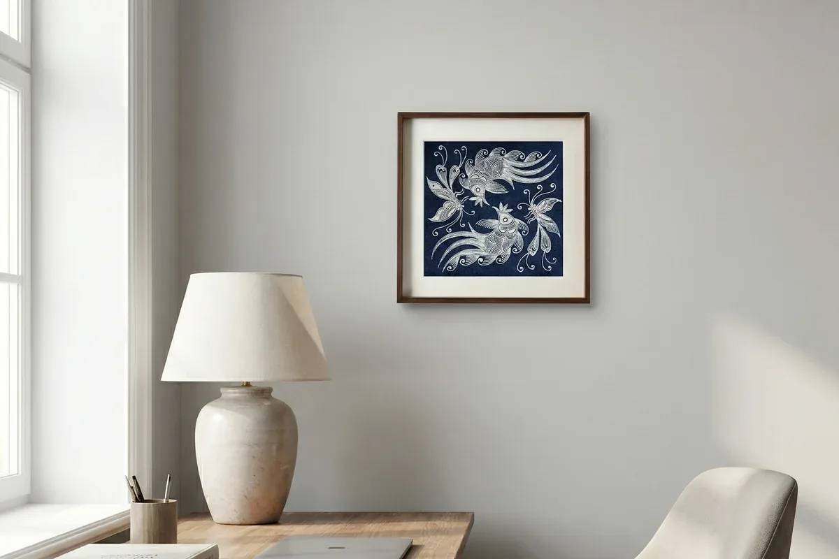 Framed indigo batik wall art hanging above a wooden desk and lamp in a light-filled room